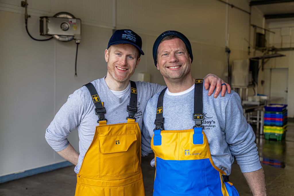 Dermot O'Leary and worker in yellow waterproofs smiling inside Molloy’s seafood facility in Killybegs harbour.