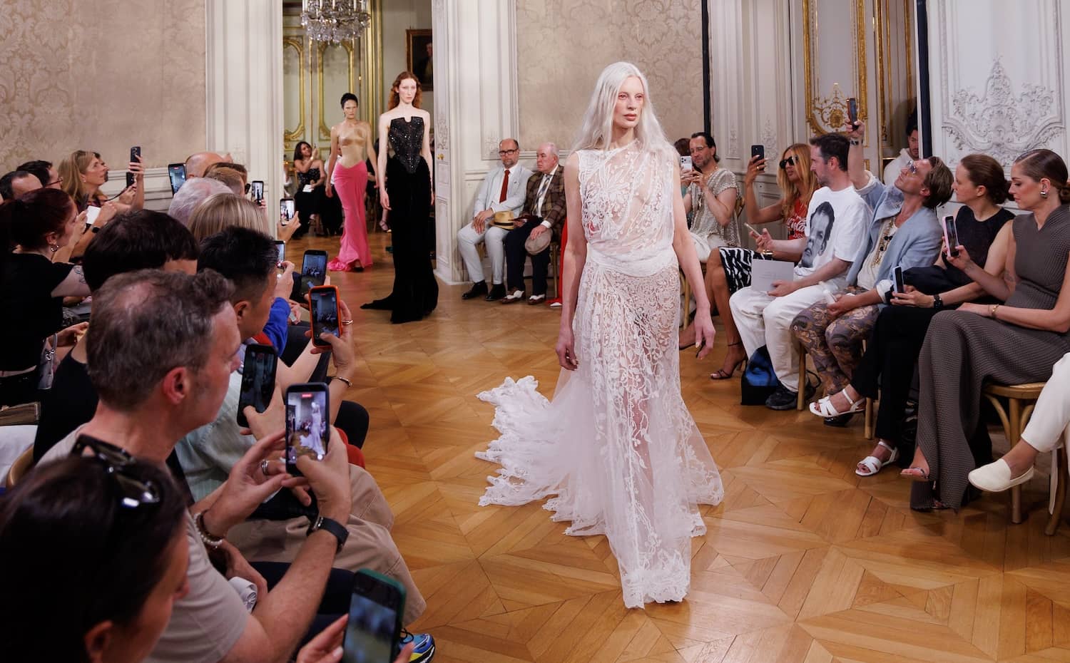 Model wearing an intricate white Irish lace gown at a fashion show.