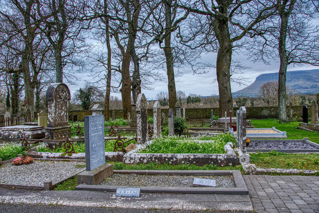 WB Yeats' grave surrounded by historic headstones and bare trees in a peaceful churchyard in County Sligo, Ireland.