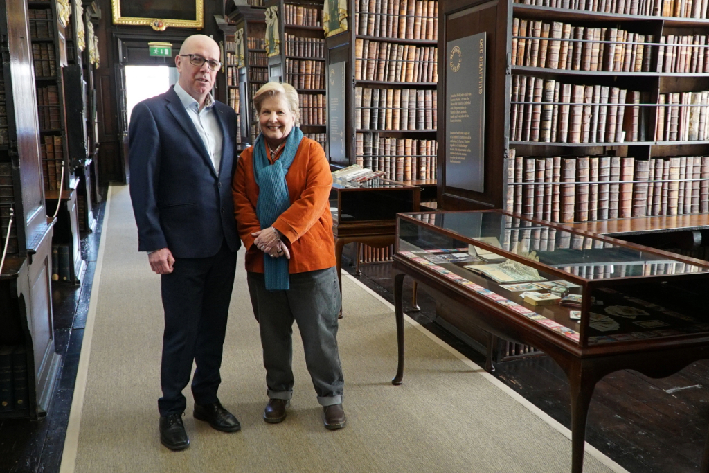 Sandi Toksvig and a man stand beside glass display cases and shelves of historic books in Marsh's Library, Dublin.