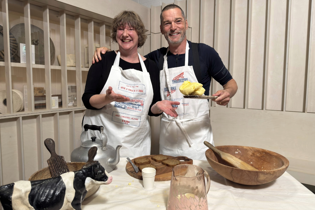 Fred and a tour guide in aprons presenting traditional butter-making tools and fresh butter inside the Butter Museum in Cork.