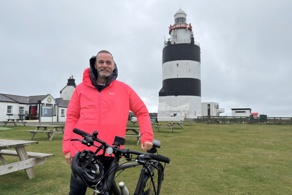 Fred standing beside a bicycle on the lawn at Hook Lighthouse, County Wexford, with the striped tower behind.