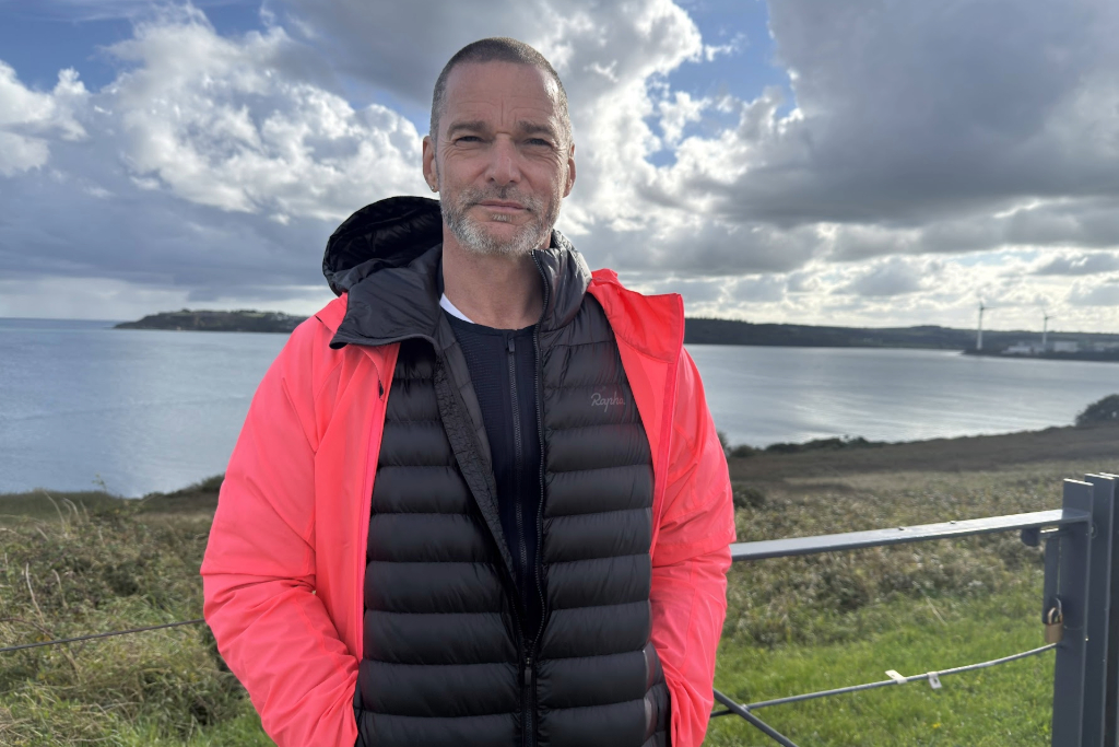 Fred in a bright jacket standing by the coastline on Spike Island, County Cork, with harbour waters behind.