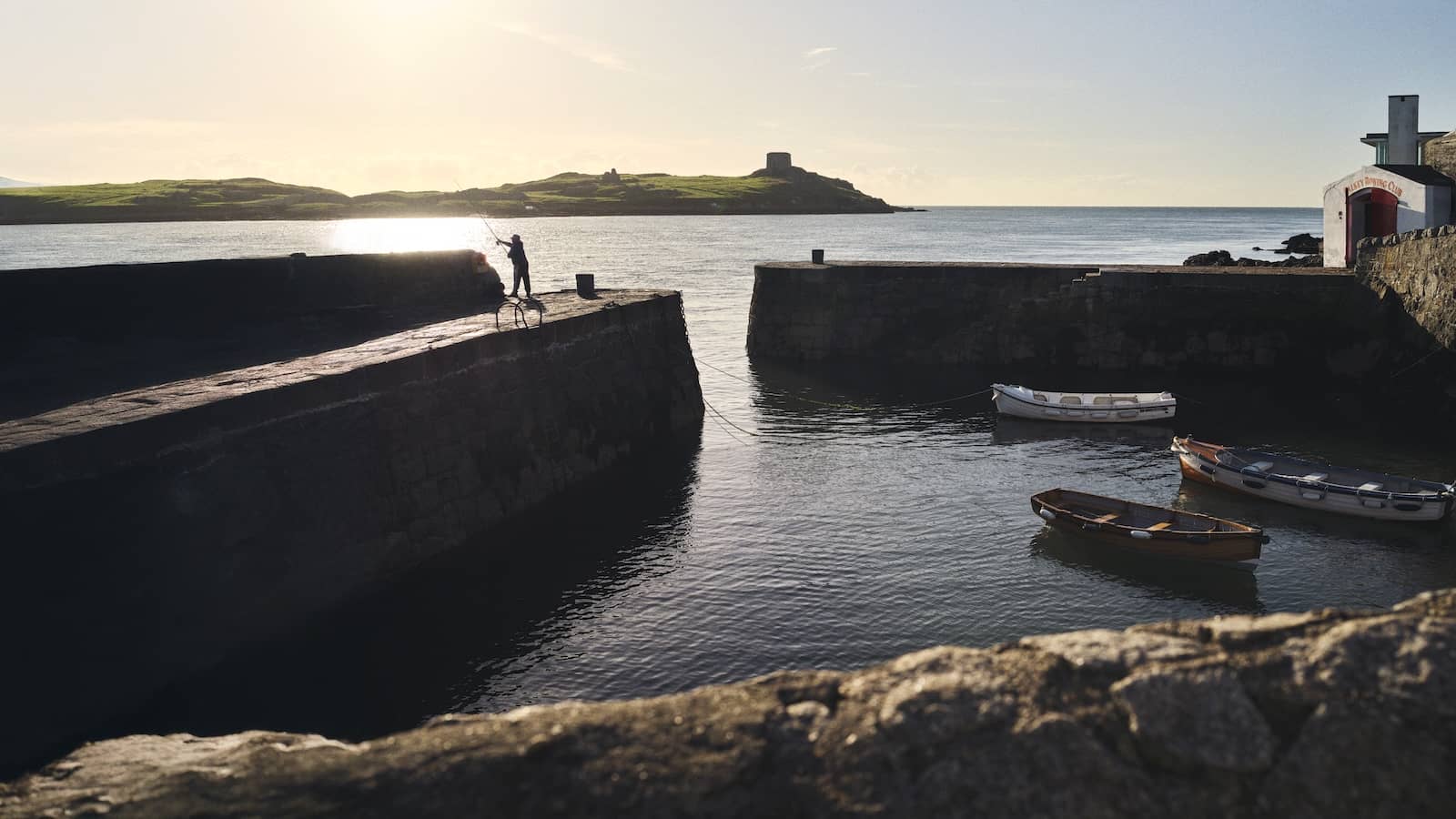 Boats moored at Colliemore Harbour in Dalkey, Dublin, with sunlit sea views and stone piers.