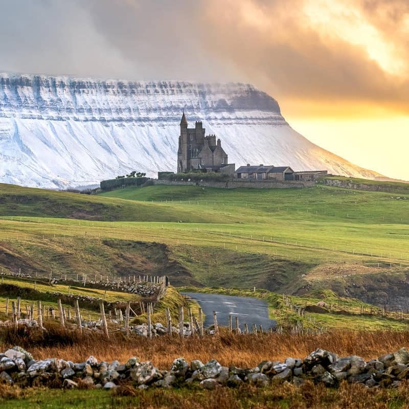 Classiebawn Castle on open fields beneath the dramatic cliffs of Ben Bulben at sunset.