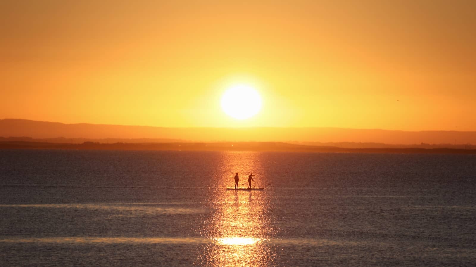 Paddleboarders drift across Galway Bay at sunset off Salthill, silhouetted in golden light.