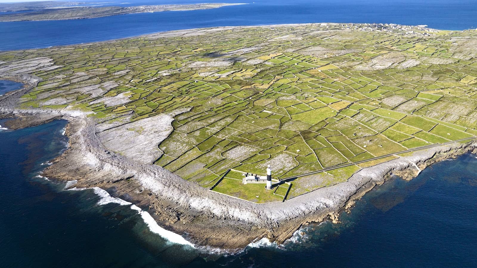 Aerial view of Inis Oírr with patchwork stone-walled fields and lighthouse along the rugged Aran Islands coastline, County Galway.