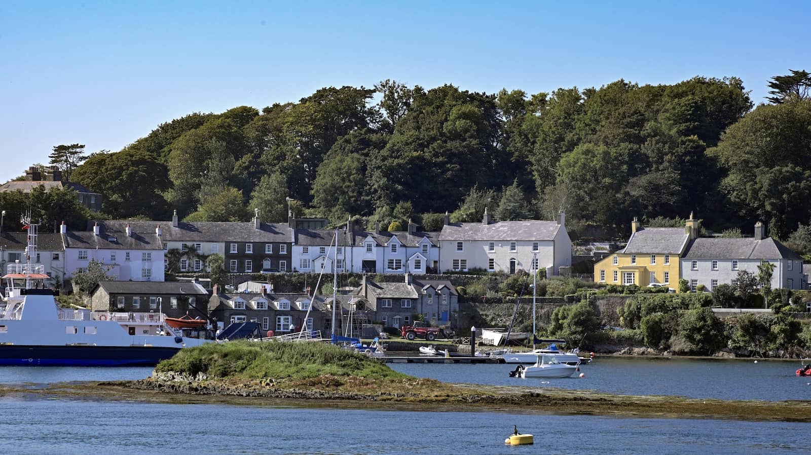 Boats and a ferry sit in Strangford Harbour with colourful village houses along the waterfront, County Down.