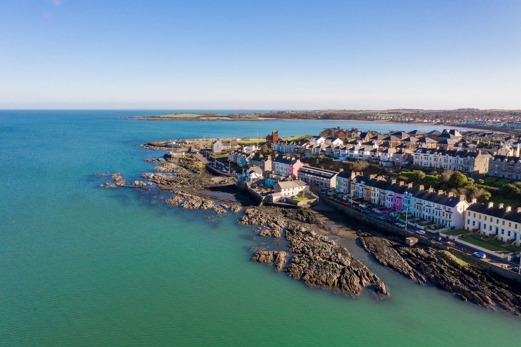 A row of colourful houses lines a rocky coastline in Bangor, County Down, backed by a sheltered bay and gentle headlands.