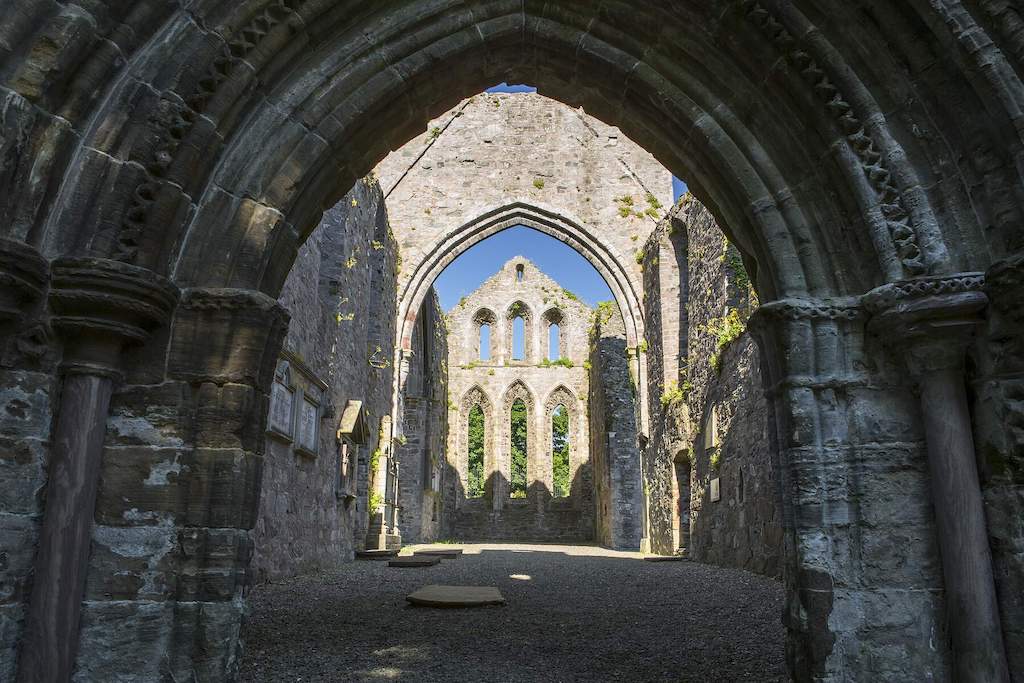 Gothic stone archways and windows of a medieval abbey ruin with sunlight filtering in.