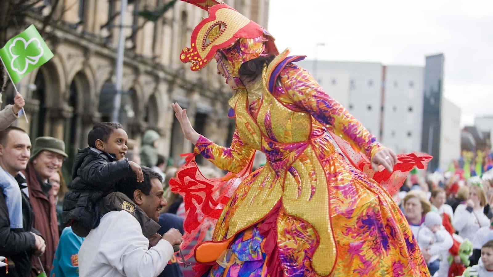 Parade performer in colourful costume high-fiving a child in the crowd, Belfast.