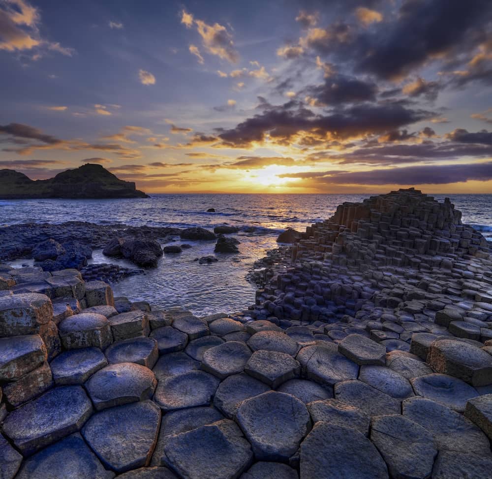 Sunset over the Giant’s Causeway, County Antrim, with hexagonal basalt stones and waves along the shore.