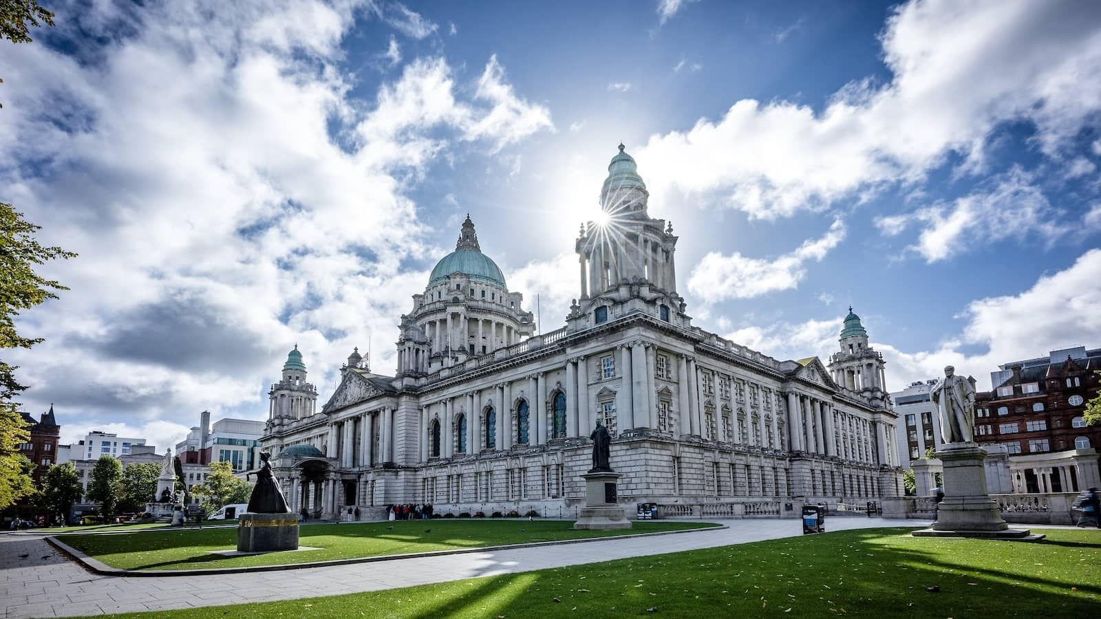 Belfast City Hall set in landscaped gardens under a bright blue sky.