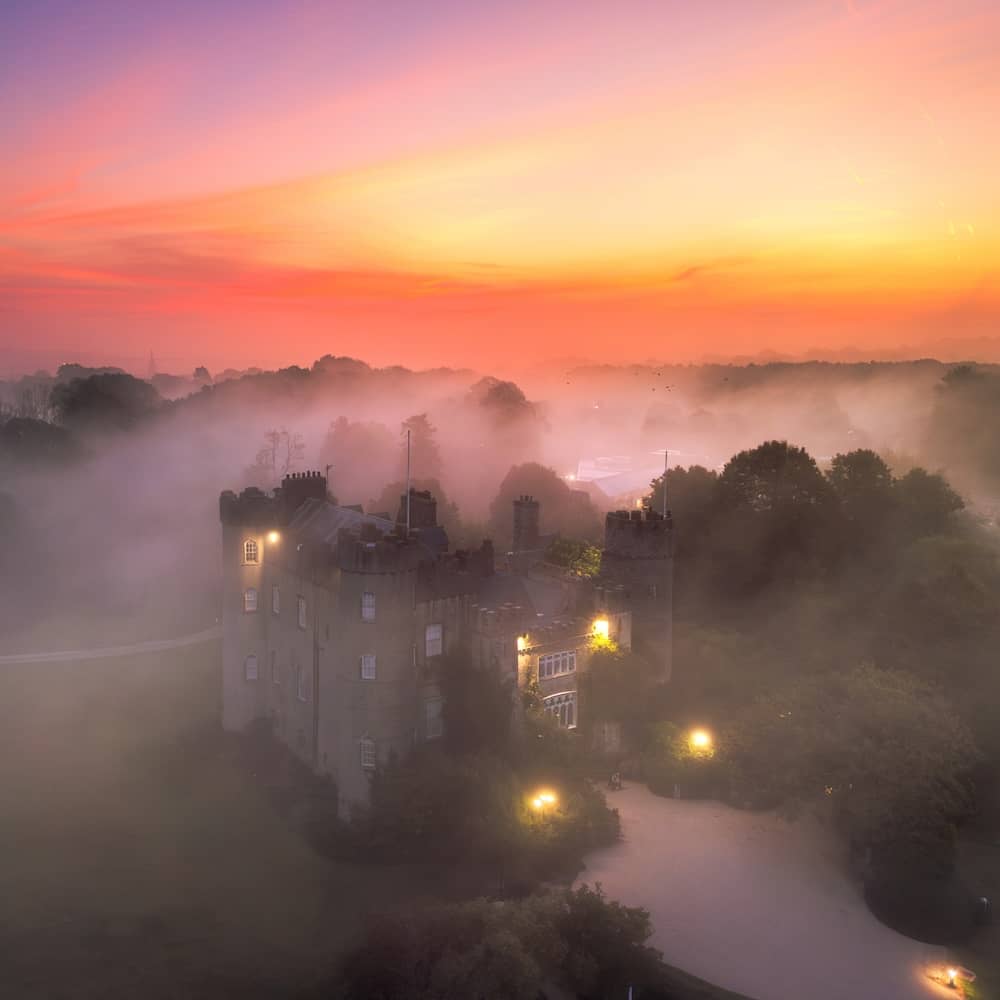 Malahide Castle, County Dublin, omgeven door mist bij zonsopgang met gloeiende lichten en een kleurrijke winterhemel.