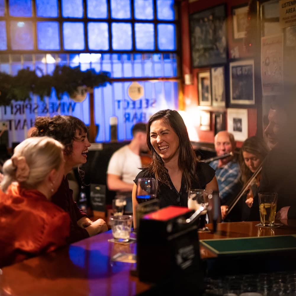 Vrienden die lachen en genieten van een drankje met live traditionele muziek in een gezellige pub in Dublin.