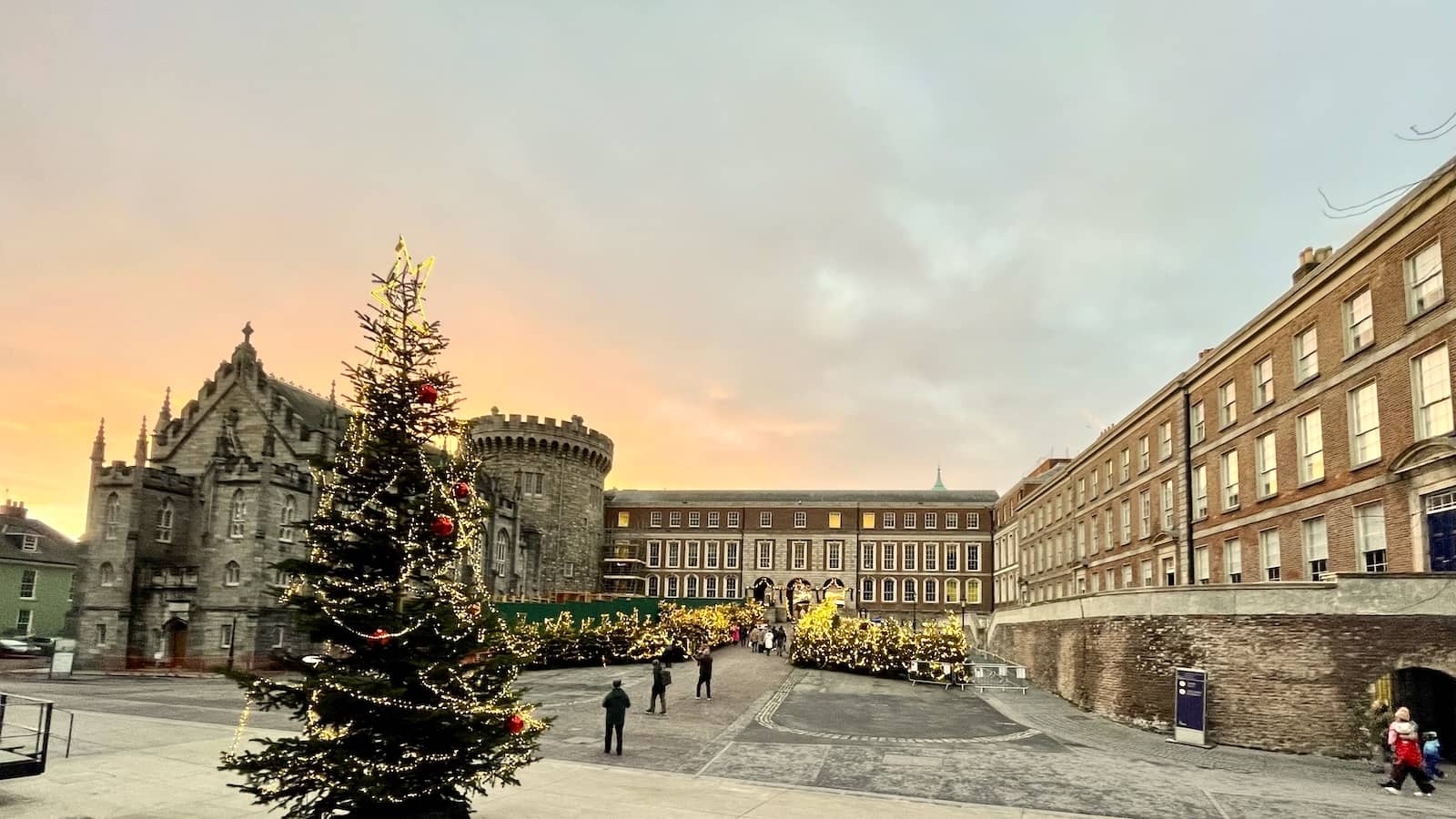 Kerstboom en feestelijke verlichting op de binnenplaats van Dublin Castle tijdens de kerstmarkt bij zonsondergang.