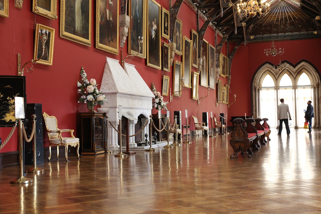 De sierlijke Lange Galerij in het kasteel van Kilkenny met rode muren, portretten, kroonluchters en een houten vloer.