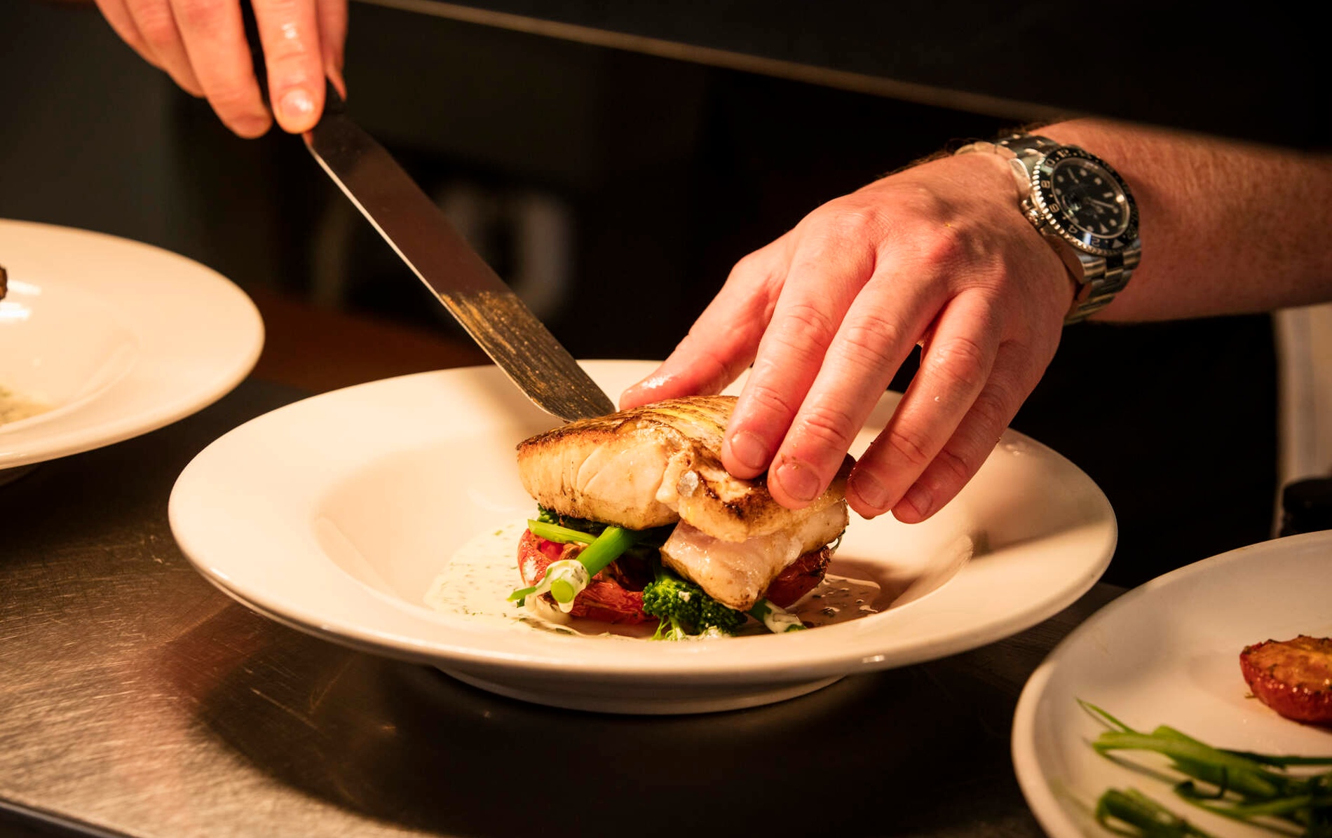 Chef plates grilled white fish on vegetables at Mourne Seafood Bar in County Down, adding sauce with care.
