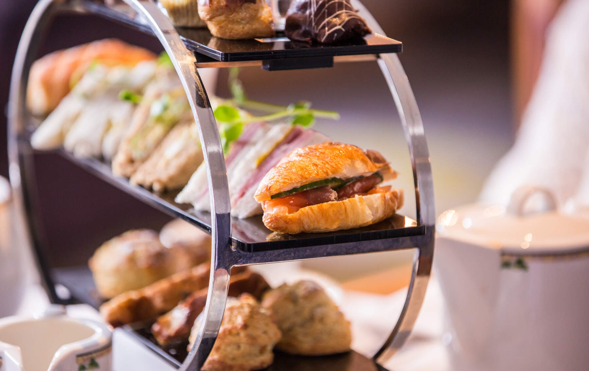 Tiered tray of croissant sandwiches, dainty finger sandwiches, and scones for afternoon tea.