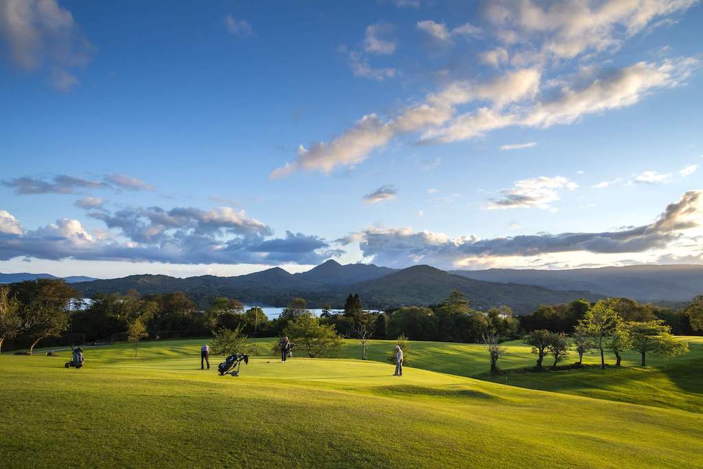 Golfer auf dem Grün des Glengarriff Golf Clubs mit Blick auf die Bantry Bay, wobei sich im Hintergrund Berge erheben.