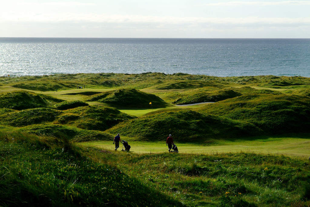 Golfer laufen über die zerklüfteten Fairways des Strandhill Golf Clubs, wobei sich der Atlantische Ozean über den Platz hinaus erstreckt.