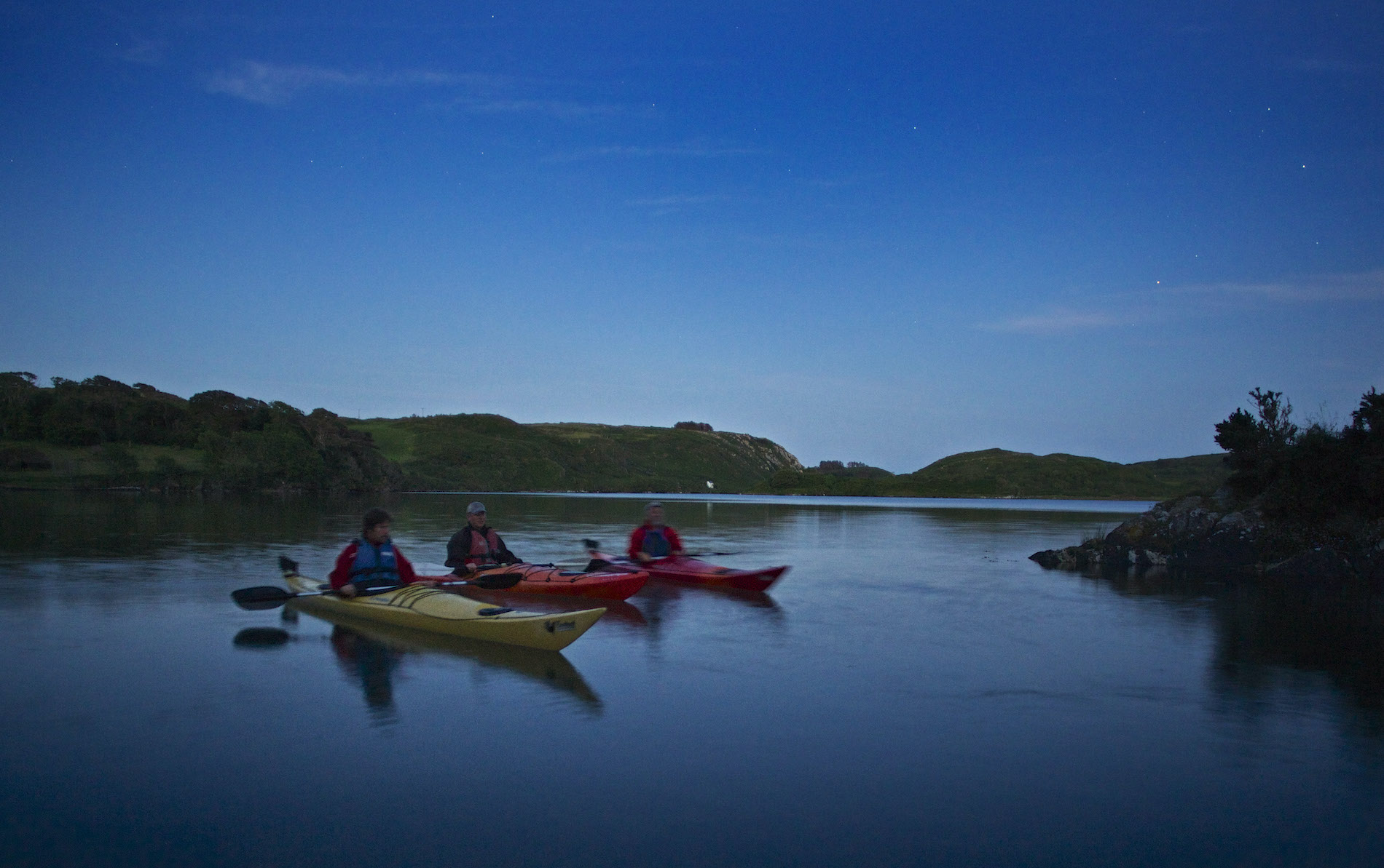 Un gruppo di persone fa kayak sotto il cielo crepuscolare sulla tranquilla Lough Hyne nella contea di Cork.