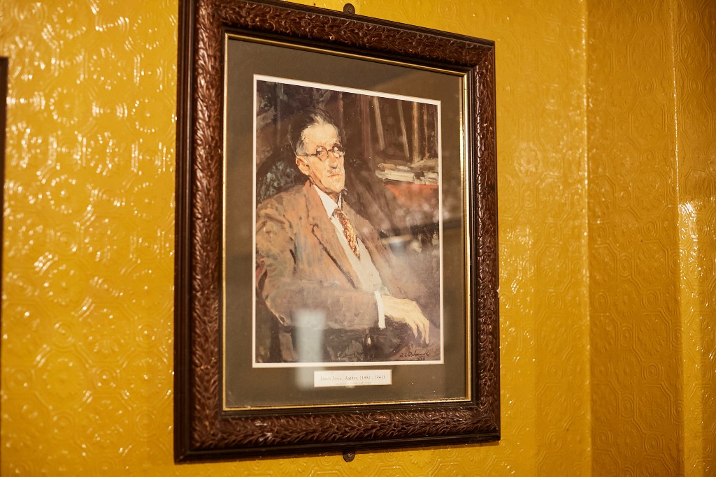 Retrato enmarcado del autor James Joyce colgado en una pared de textura dorada en un tradicional pub de Dublín.