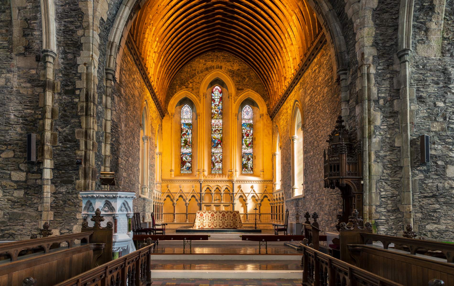 Interior of St Brigid’s Cathedral in Kildare, with vaulted wooden ceiling, stone walls and a stained-glass window above the altar.