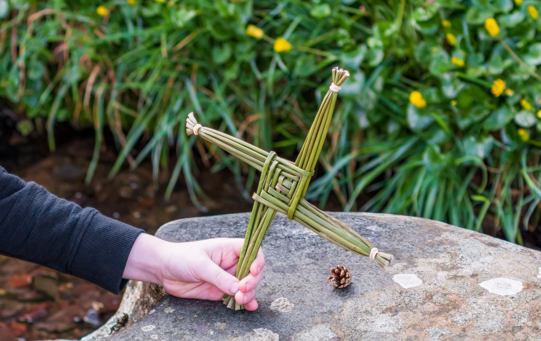 Person holding a traditional Saint Brigid’s cross made of rushes over a granite well at a shrine in County Louth.