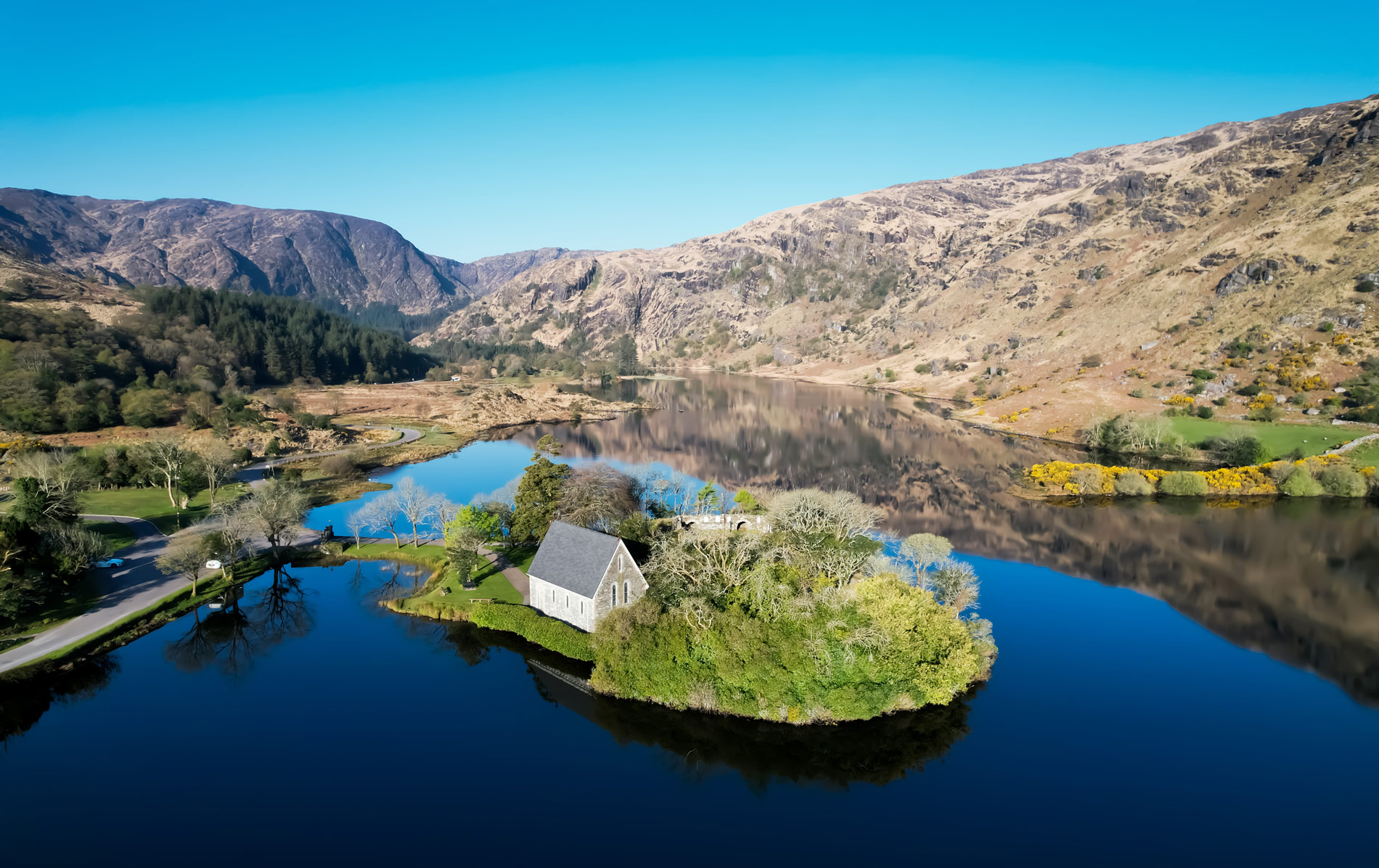 St Finbarr’s Oratory reflected in Gougane Barra Lake, set against mountains in County Cork.