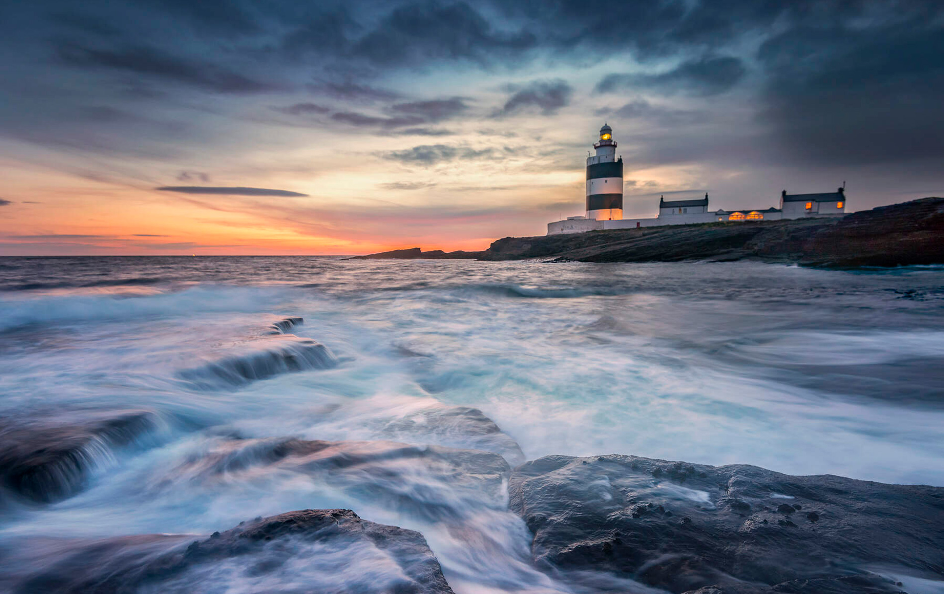 Hook Lighthouse at sunset with waves crashing on rocks, County Wexford.