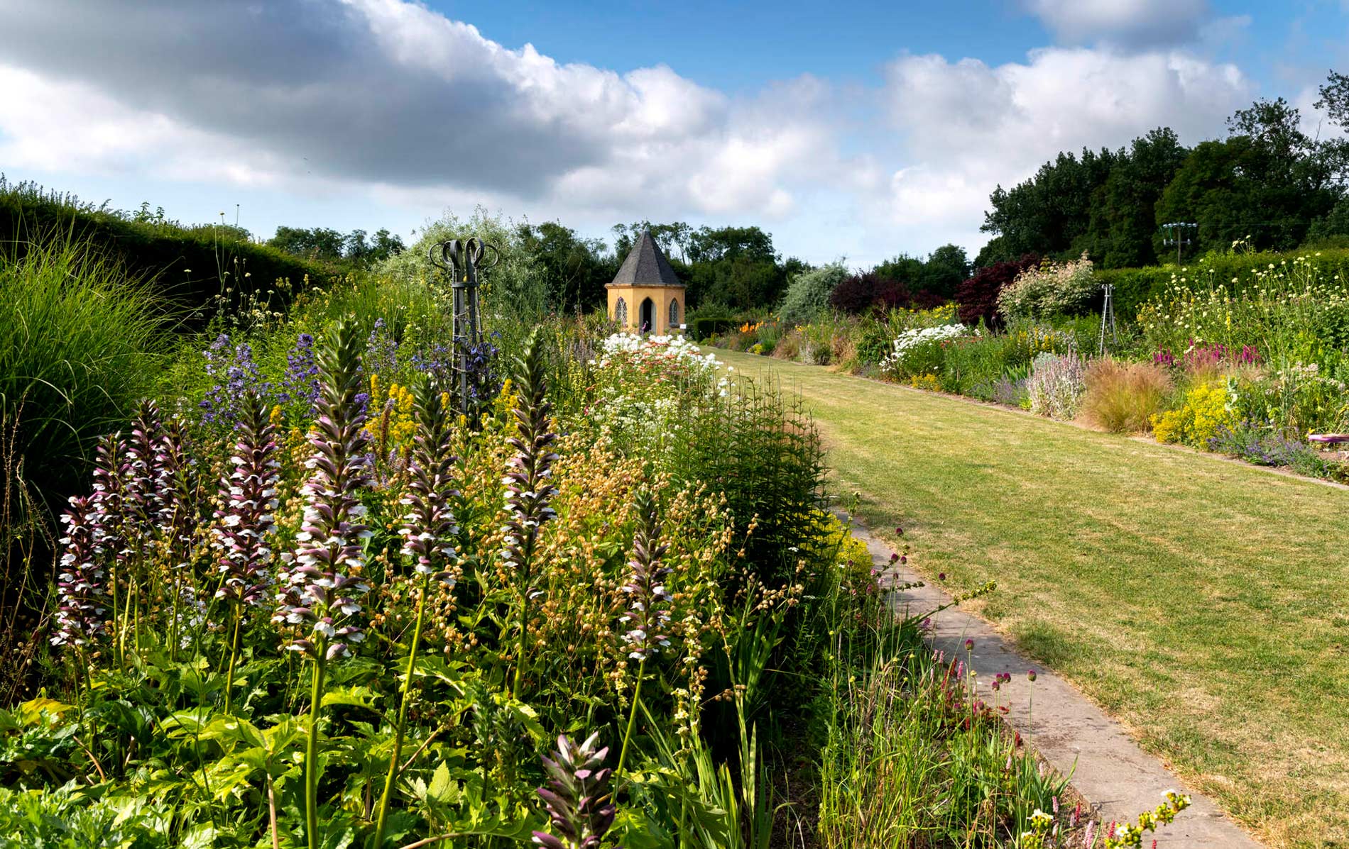 Colourful flower borders lining a garden path leading to a small pavilion in Ireland.