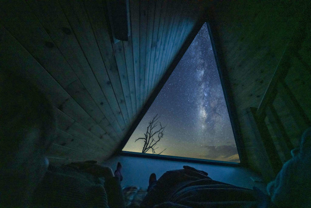 La Vía Láctea visible a través de una ventana triangular encima de una cama en una oscura cabaña de madera en el condado de Tyrone.