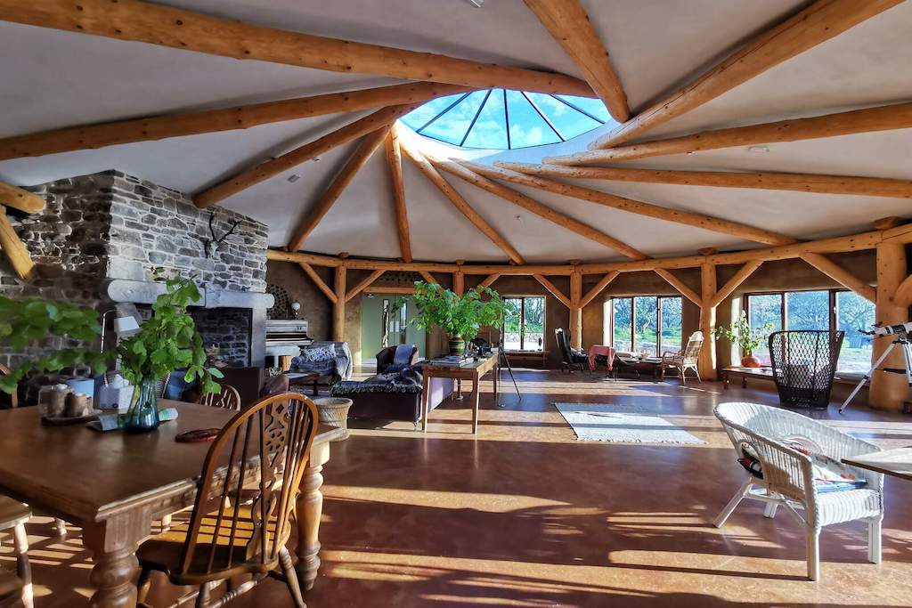 Interior amplio de un hotel ecológico con vigas de madera natural, chimenea de piedra y vistas al bosque en el condado de Donegal.