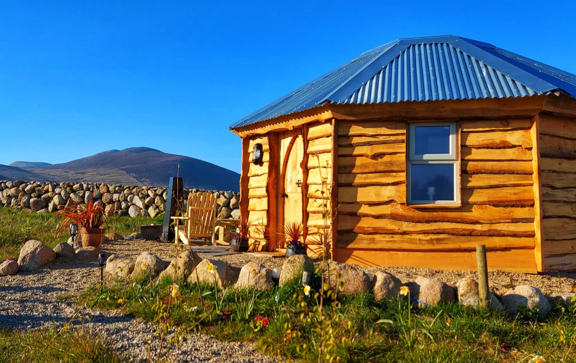 Willow Tree Glamping cabin with corrugated roof and outdoor chairs set against a mountain backdrop in County Down.
