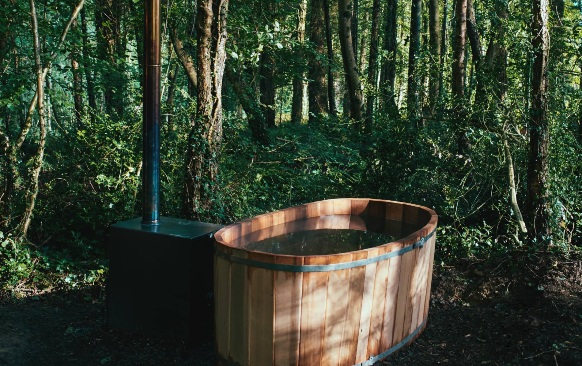 Unoccupied wooden hot tub with chimney nestled among tall trees at Cabü By the Lakes, County Cavan.