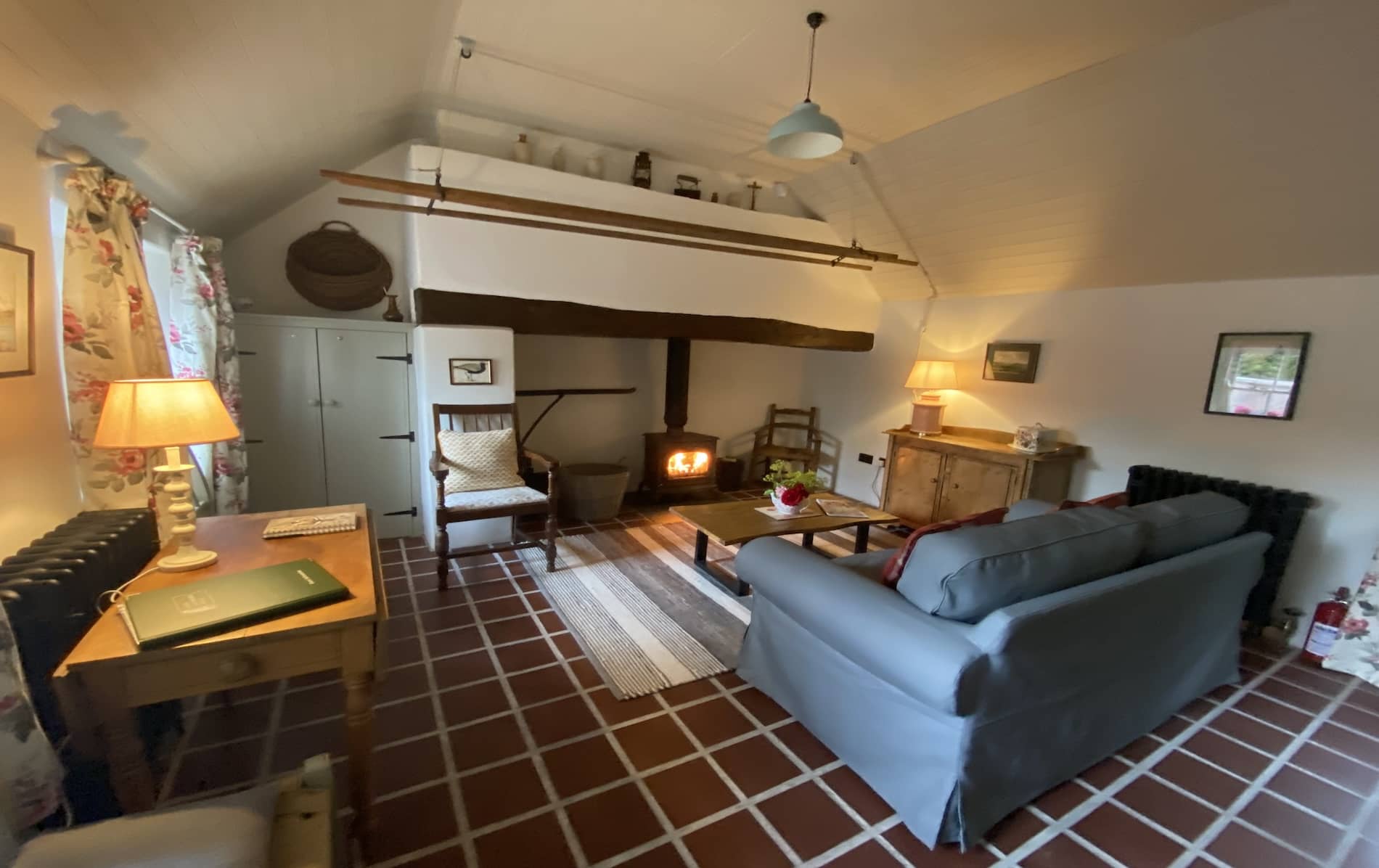 Kilkee Cottage interior with wood-burning stove, tiled floor, curtains, and vintage wooden and cushioned furniture in Cork.