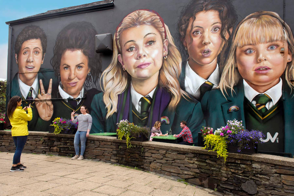Los turistas posan para fotos frente al colorido mural de las chicas de Derry en una pared de fachada en Derry~Londonderry.
