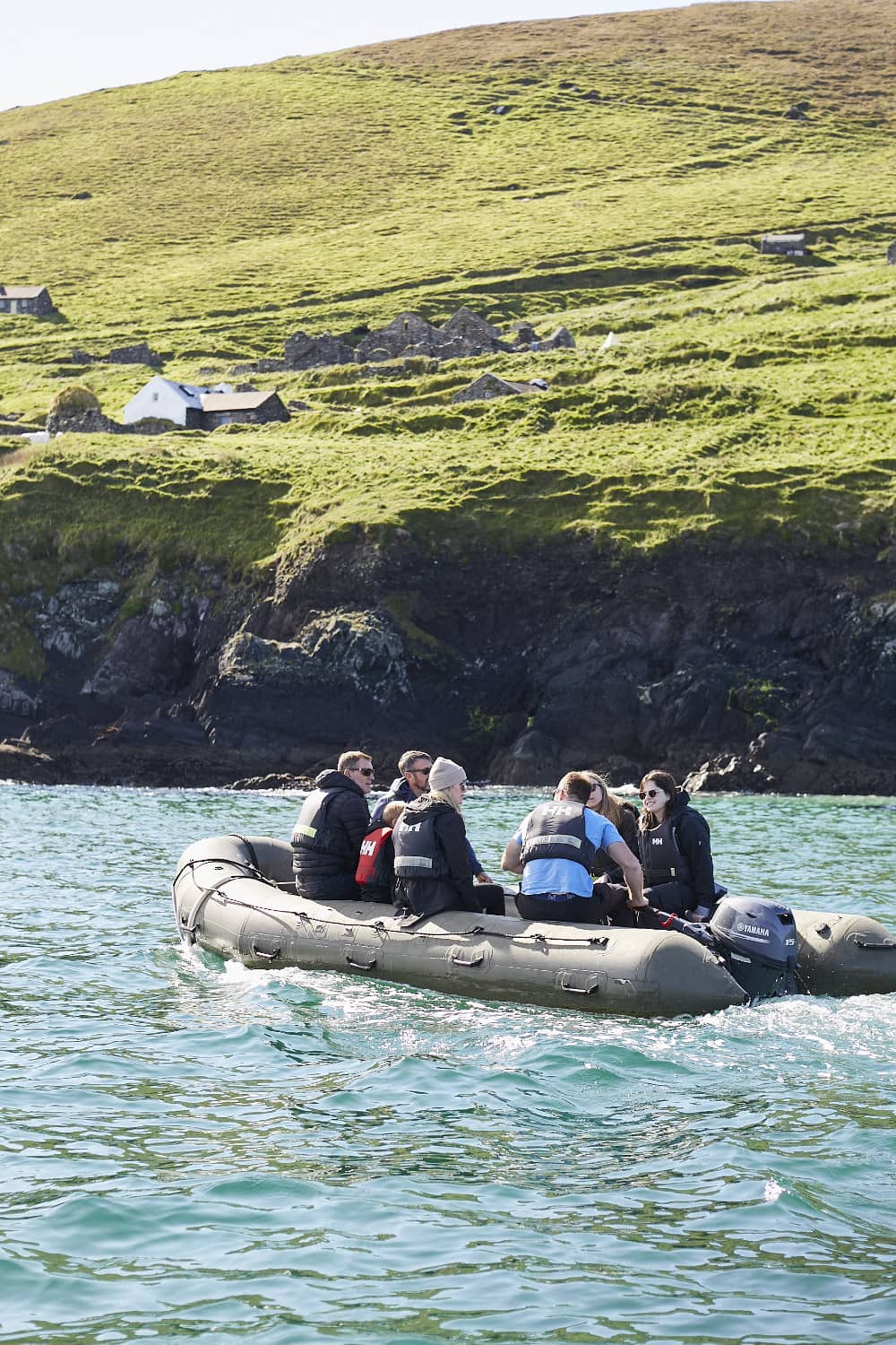 Grupo de visitantes con chalecos salvavidas a borde de una lancha RIB frente a la isla Great Blasket, con colinas verdes y ruinas visibles.