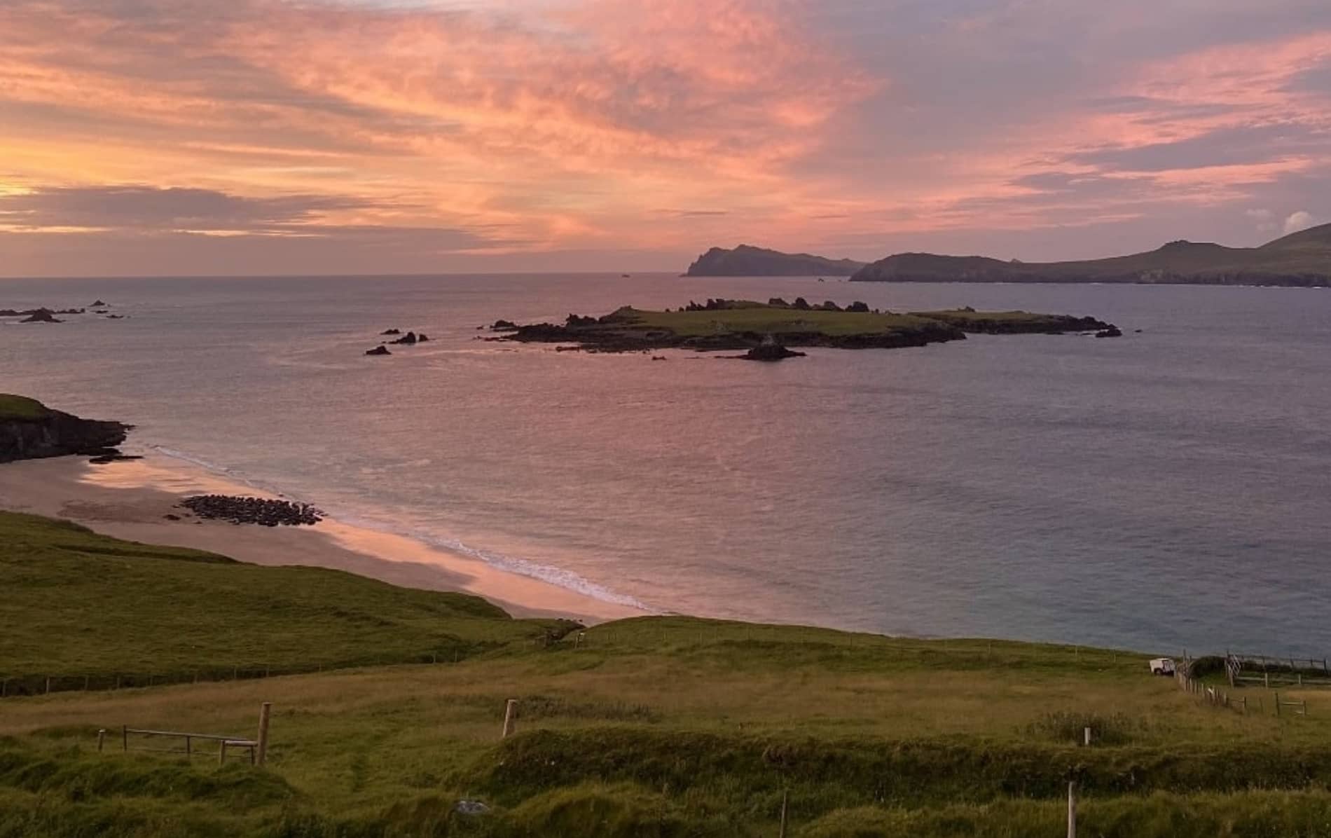 Vista del Océano Atlántico y las islas circundantes al atardecer desde la Isla Great Blasket, con un cielo rosa y olas tranquilas en la costa.