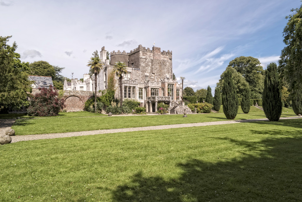 Huntington Castle surrounded by manicured lawns and cypress trees, with stone battlements and a palm tree.