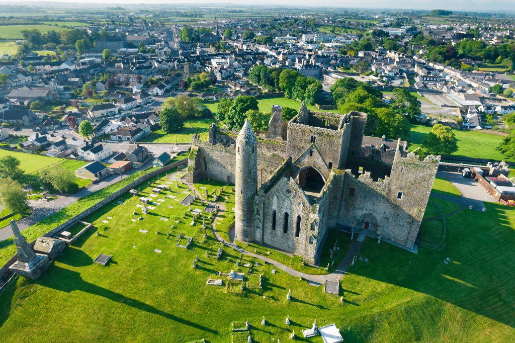 Aerial view of the Rock of Cashel and its round tower, overlooking a graveyard and the rooftops of the surrounding town.