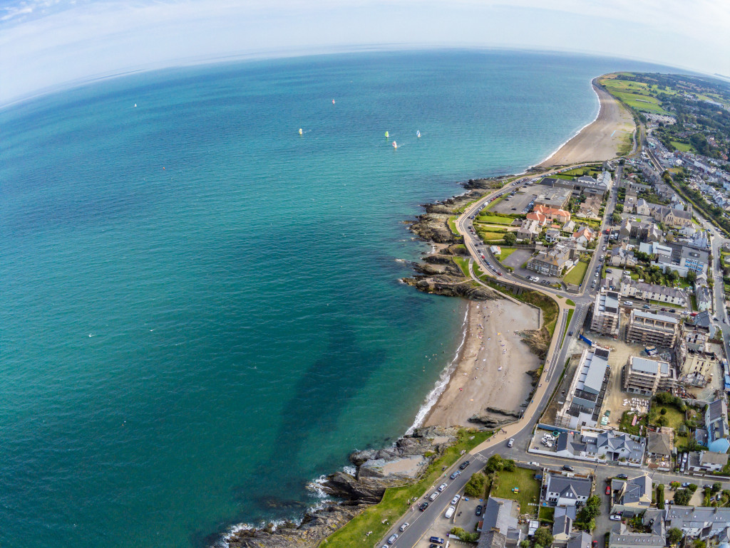 Aerial view of Greystones showing its curved coastline, sandy beach, and colourful rooftops along the seafront.