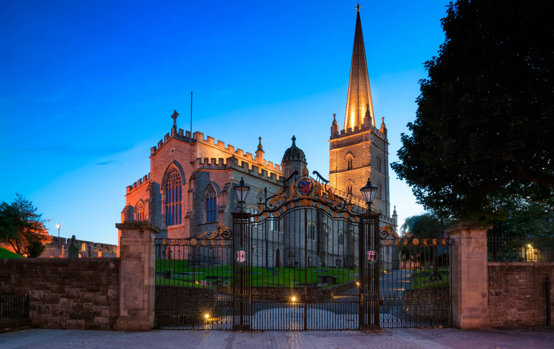 St Columb’s Cathedral glowing at twilight, framed by ornate wrought iron gates in Derry~Londonderry.