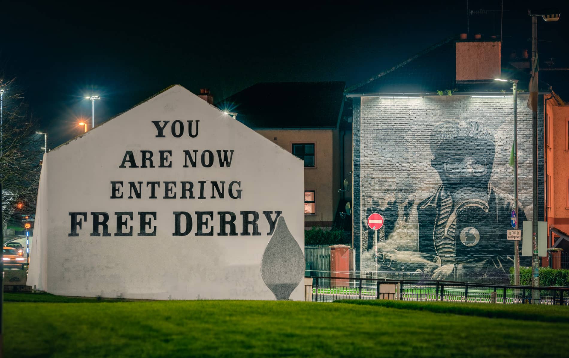 Illuminated Free Derry Corner sign and peace mural in the Bogside area of Derry at night.