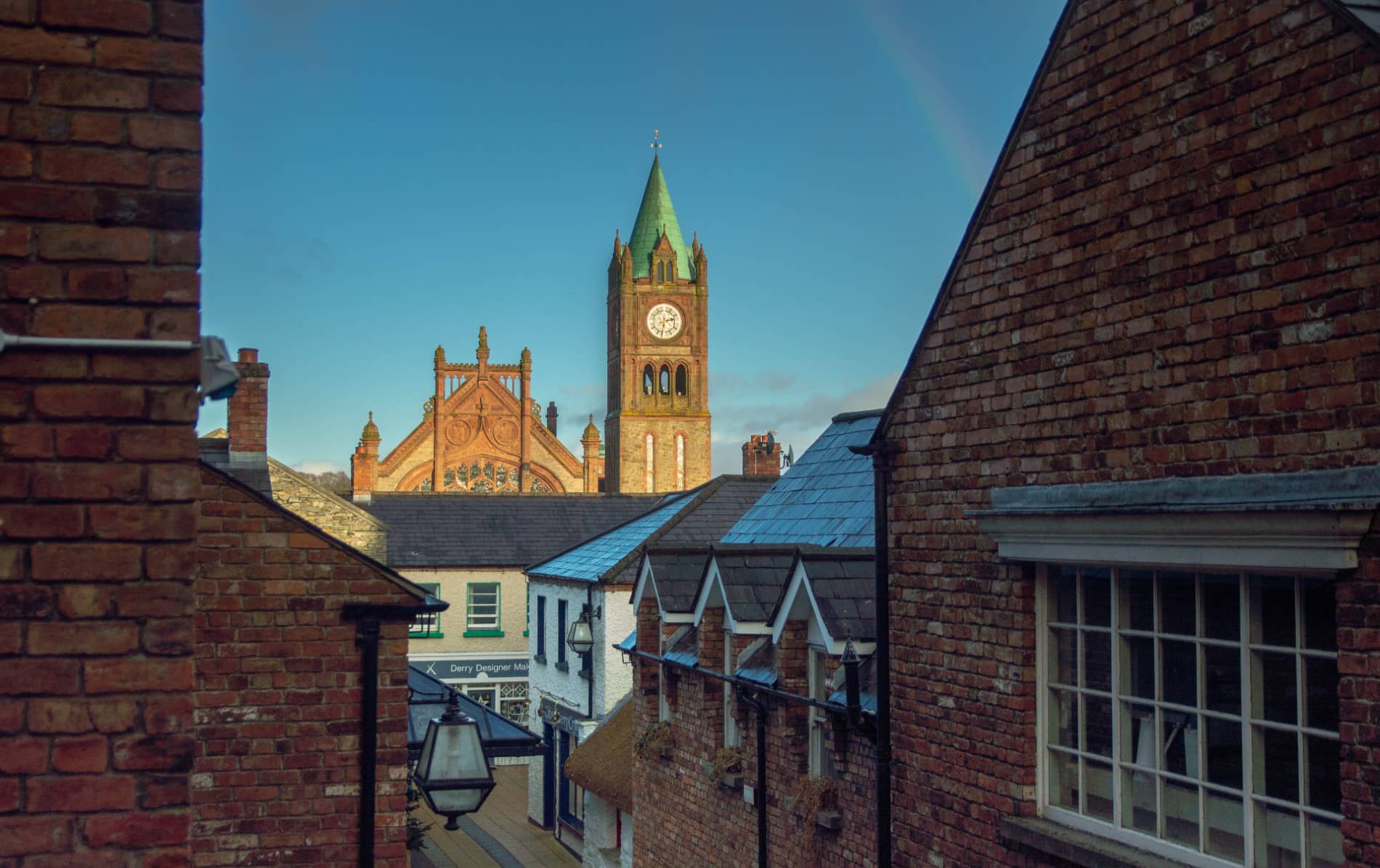 Guildhall clock tower seen above rooftops in Derry’s Craft Village with a morning sky overhead.