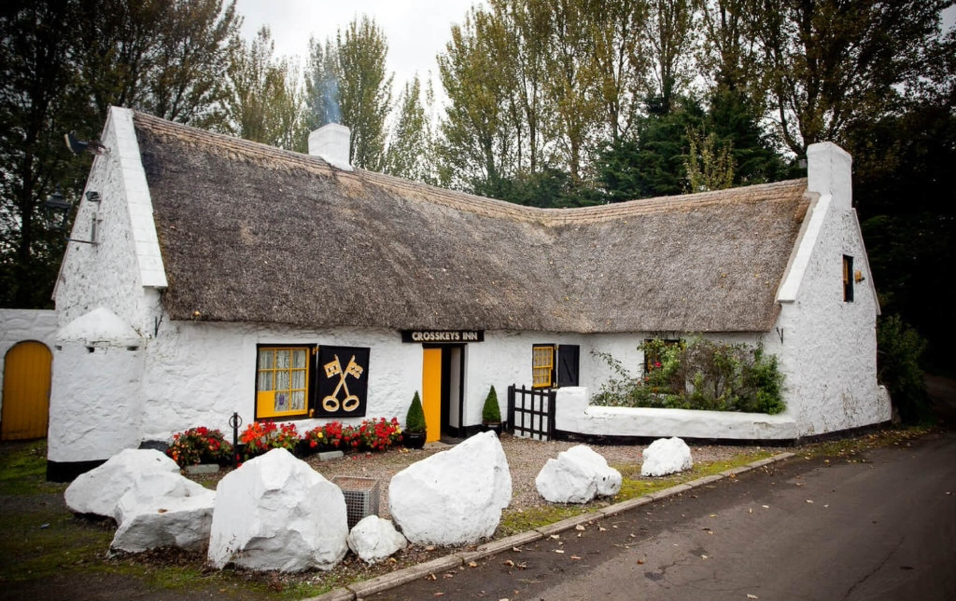 Historic thatched Crosskeys Inn with white walls, yellow windows, and floral displays in Antrim.