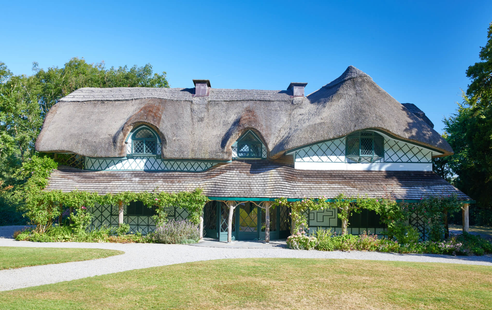 Decorative thatched Swiss Cottage with ornate windows and climbing plants in landscaped gardens in Tipperary.