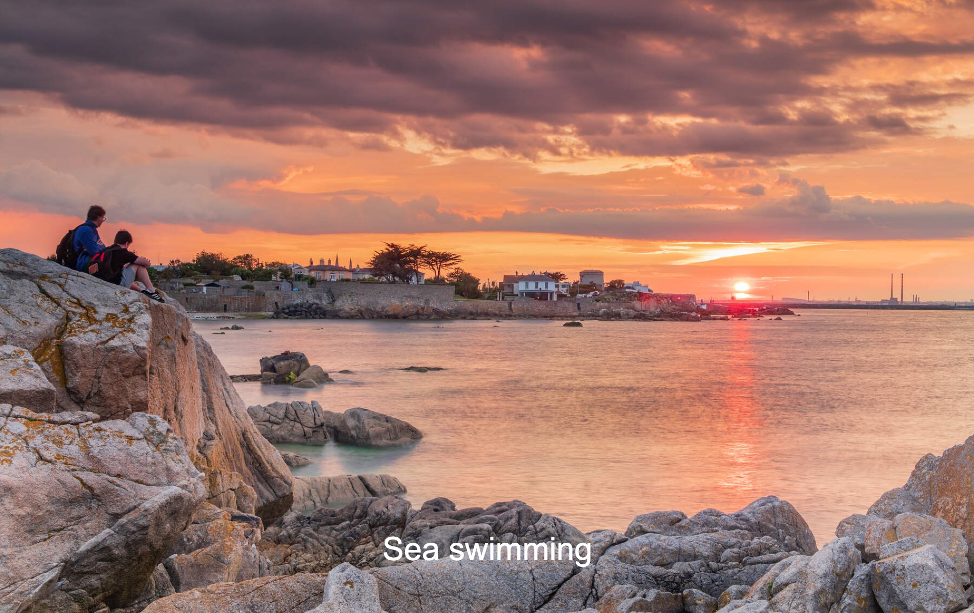 People watching the sunset over Dalkey, County Dublin, with rocky shoreline.