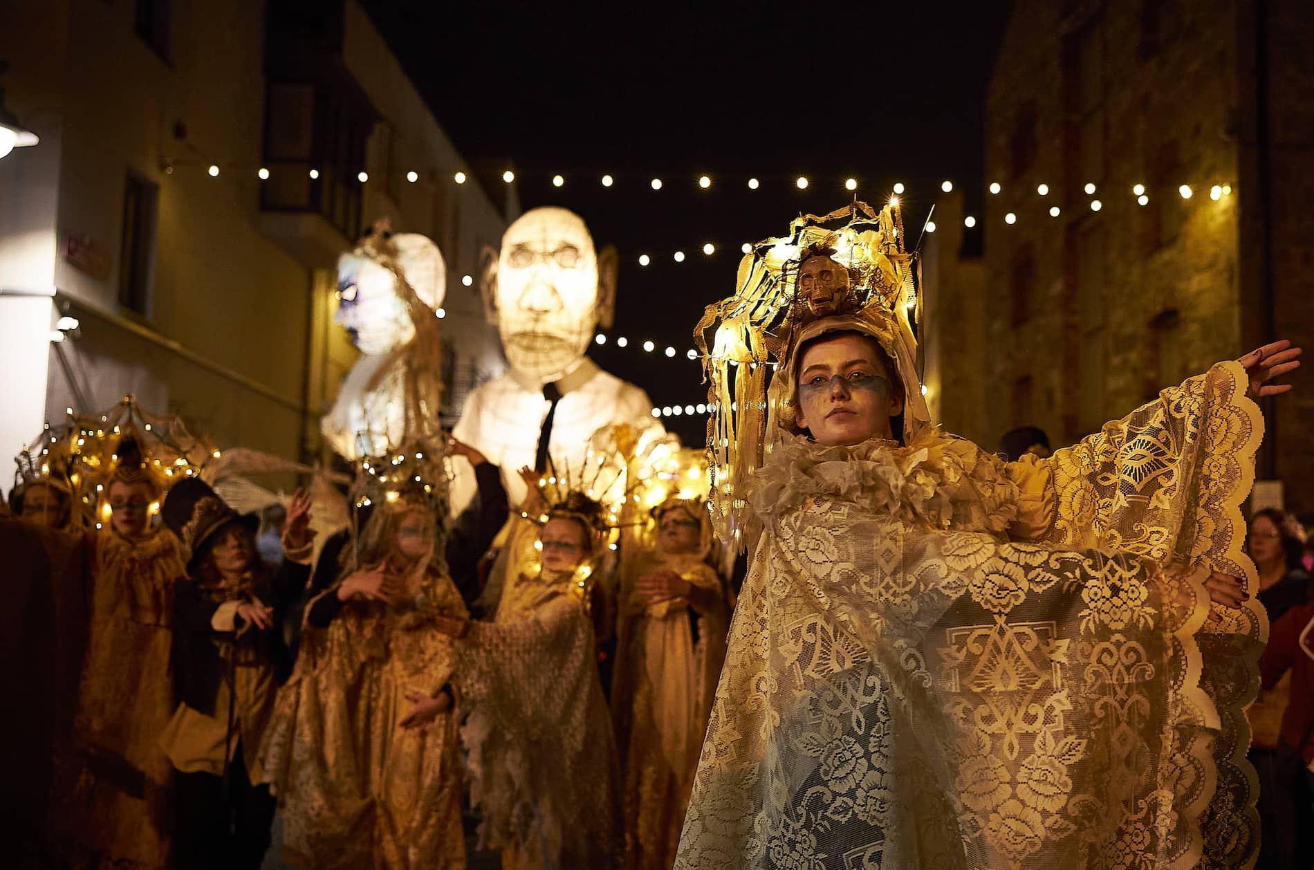 Ein Darsteller in einem kunstvollen Spitzenkostüm mit leuchtendem Kopfschmuck führt die nächtliche Halloween-Parade mit riesigen Laternenpuppen in Limerick an.